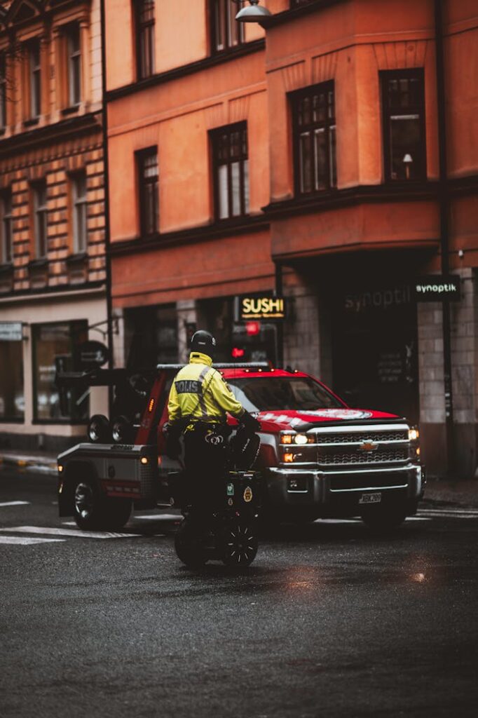 Urban setting with police patrol on Segway and a tow truck parked on a wet city street.