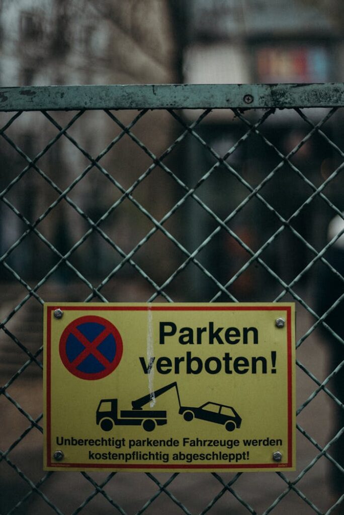 German "No Parking" sign on a chain-link fence in an urban setting.